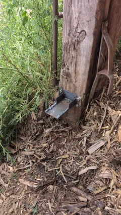 Fabricated gate support bracket bolted to the wooden post, a cradle that carries the gate weight when closed