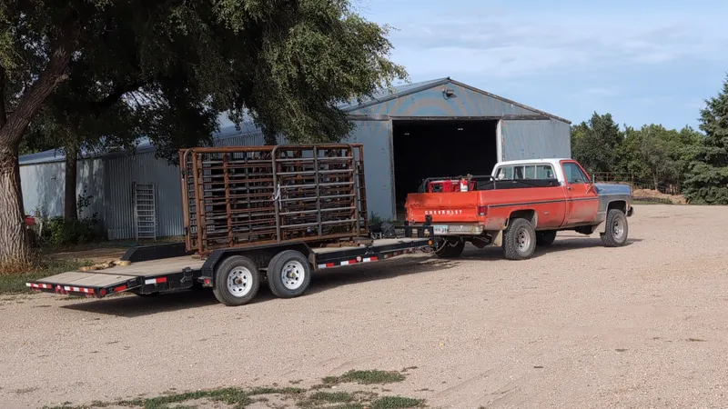 Stack of finished free-standing panels with gates loaded on a flatbed trailer behind an orange squarebody Chevy, ready for delivery to the calving barn