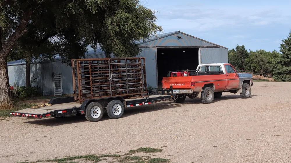 Stack of finished free-standing panels with gates loaded on a flatbed trailer behind an orange squarebody Chevy, ready for delivery to the calving barn